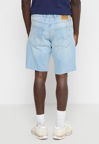 Lichtblauwe denim shorts met een rechte snit, voorzien van dubbele achterzakken en een tan label op de tailleband. gedragen met witte sokken en sneakers.