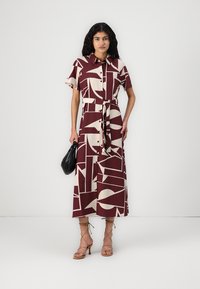 Robe chemise bordeaux avec un motif géométrique abstrait crème, manches courtes, devant à boutons, ceinture à la taille, et sandales à lanières avec liens à la cheville.