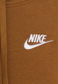 Nike hoodie i brunt tyg med en slät textur. Har en broderad vit logotyp framtill. Enkelt design och rundad hals.