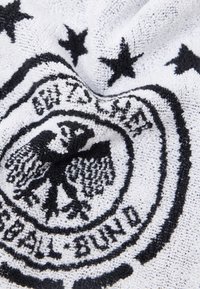 Sort ørn emblem med stjerner og teksten "Bundesliga" på en tekstureret hvid stofbaggrund.