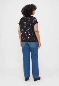Black floral blouse with short sleeves, featuring pink and green patterns. Paired with high-waisted blue jeans and black chunky heels.