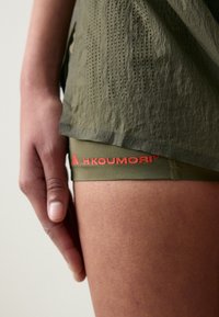 Maslinasto zelene atletske kratke hlače s perforiranim dizajnom i H.KOUMORI logotipom u narančastoj boji na elastičnom pojasu. Glatka tekstura i prilagođen oblik.
