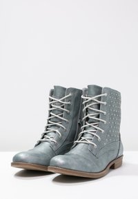 Botines con cordones en cuero azul claro con acentos perforados, puntera redonda y cordones gris claro, que cuentan con un tacón de madera bajo.