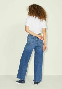 Jean large taille haute bleu en denim, avec poches arrière et coupe décontractée, associé à un T-shirt blanc et des baskets.