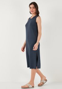 Laivansinisettömä sleeveless-mekko, jossa on sivuleikkaukset, pehmeästä kankaasta valmistettu ja polven alapuolelle ulottuva, yhdistettynä hopeanvärisiin sandaaleihin.