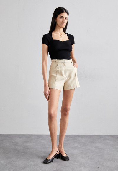 Zwart geribbeld T-shirt met korte mouwen en vierkante halslijn; beige op maat gemaakte shorts met zijzakken; zwarte slingback schoenen met gouden accenten.