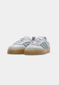 Sneakers bianchi con strisce verdi, realizzati in materiali scamosciati e in pelle, punta tonda e suola in gomma testurizzata. Presentano lacci e linguetta imbottita.