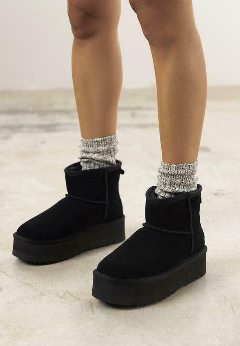 Botines de ante negros con suela de plataforma, con un diseño sencillo, textura suave, y combinados con calcetas de canalé grises.