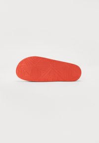 Suela de zapato de goma roja con una superficie texturizada que presenta patrones geométricos y un diseño angular para mejorar el agarre y la tracción.