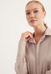 Camicia a maniche lunghe rosa chiaro con colletto, caratterizzata da una texture liscia, una leggera lucentezza e dettagli con bottoni sui polsini.