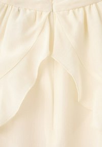 Tissu crème avec détails superposés et froncés ainsi qu'une texture subtile, montrant la partie supérieure centrale d'un vêtement.