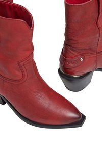 Botas de tobillo de cuero rojo con punta afilada, superficie texturizada y tacón cuadrado negro. Incluye un diseño cosido y un acento de logotipo.