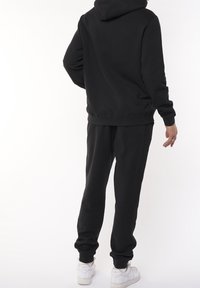 Svart huvtröja och sweatpants-set, med en avslappnad passform, ribbade muddar och en dragskohuva, kombinerat med vita träningsskor.