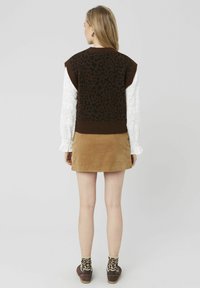 Gilet en maille marron avec motif léopard noir, associé à une chemise blanche à manches longues en dentelle et une mini-jupe en velours côtelé beige. Chaussures marron.