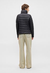 Juodas pūkinis paltas su vertikaliu siuvinėjimo dizainu, aukšta apykakle ir lygiu paviršiumi, dėvimas su šviesiai bežinėmis plačiomis kelnėmis.