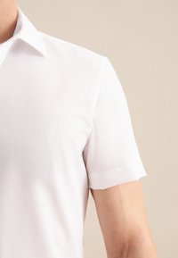 Korte mouwen witte shirt met een puntige kraag en een gladde textuur. Bevat een gestreepte onderkraag en heeft een relaxte fit.