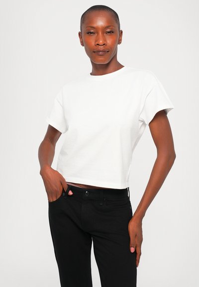 Cropped white cotton T-shirt with short sleeves, paired with black jeans. The fabric appears smooth with a basic design and no visible patterns.