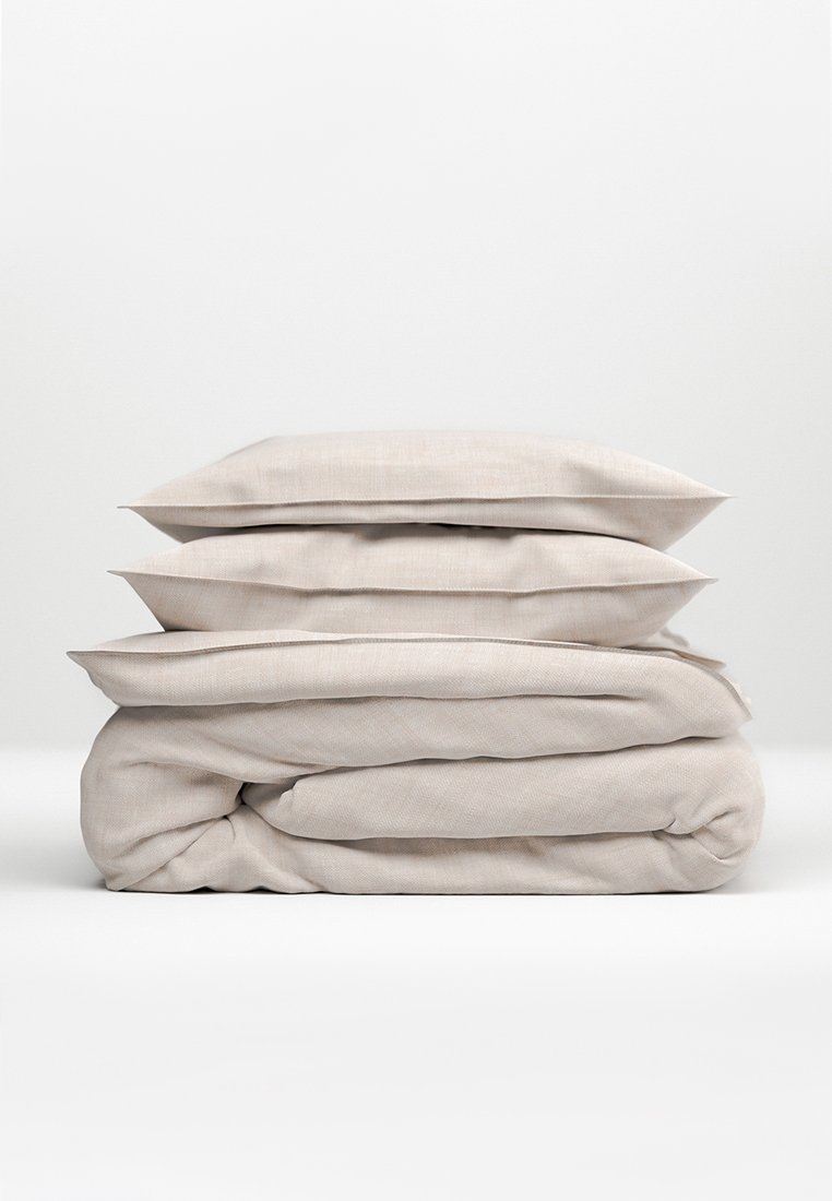 Ensemble de literie beige clair empilé avec deux coussins texturés et une couette, présentant un matériau doux, semblable à du lin. Bords soignés, design minimaliste.