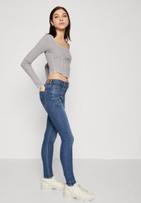 Grå langermet crop topp med sømdetaljer, parret med blå skinny jeans som har lommer foran og bak, brukt med beige sneakers.