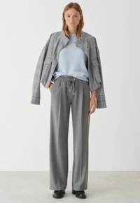 Gray wide-leg trousers with drawstring waist, paired with a light blue sweater and a checkered cropped jacket in black and white.