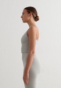 Top corto gris y leggings de cintura alta, hechos de una tela suave y elástica. Diseño simple con tirantes finos y sin patrones visibles.