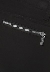Gros plan d'une poche en tissu noir avec une fermeture éclair métallique argentée horizontale et une boucle de ceinture cousue au-dessus.