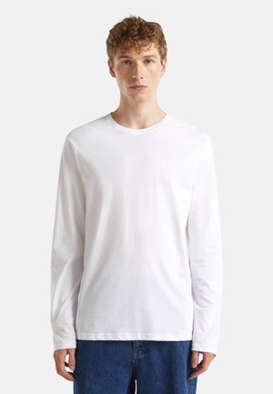 Long-sleeve white T-shirt in soft cotton, featuring a crew neckline and straight hem. Paired with loose blue denim jeans.
