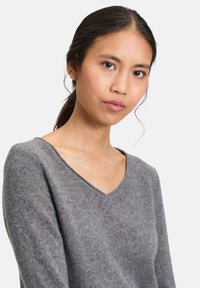 Szary sweter z dekoltem w serek, wykonany z miękkiego materiału, dopasowany krój oraz długie rękawy; subtelna tekstura widoczna w całym materiale.