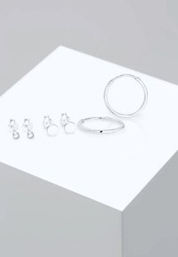 Ensemble de boucles d'oreilles en argent comprenant deux paires de boucles d'oreilles à clous et une grande boucle d'oreille, avec des finitions polies et des designs simples.