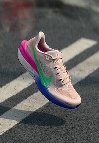 Hellrosa Sportschuh mit Mesh-Obermaterial, gestaltet mit einem grünen Swoosh und lila Akzenten an der Sohle. Schnürdesign mit dezenten Texturen.
