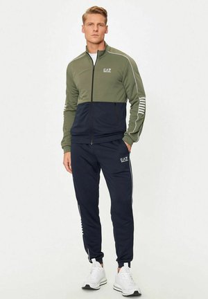 Tuta composta da una giacca con zip in verde oliva e blu navy, con accenti bianchi. Presenta pantaloni blu navy abbinati con dettaglio del logo.