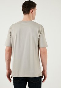 Šedé tričko s krátkým rukávem a kulatým výstřihem, vyrobené z měkké bavlněné tkaniny. Má hladký design a je kombinováno s tmavými džíny.
