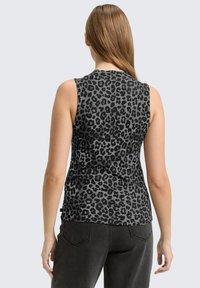 Kobieta z długimi włosami, ubrana w szary bezrękawnik z czarnym nadrukiem w panterkę i czarne dżinsy, pokazana od tyłu na prostym tle.