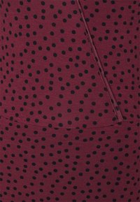 Tecido bordeaux com uma textura suave, apresentando bolinhas pretas espaçadas de forma uniforme. Inclui um detalhe de costura lateral.