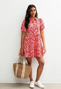Röd blommig klänning med korta puffärmar, figursydd byst och utsvängd kjol. Tillsammans med en vävd halmhandväska och vita sneakers.