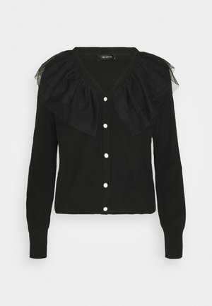 Cardigan noir à manches longues avec des boutons blancs et un grand col en tulle froufrouté le long des épaules et de l'encolure.