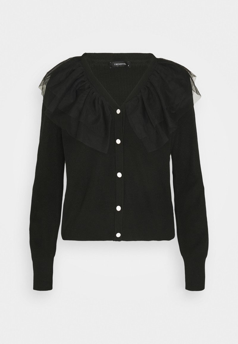Cardigan noir à manches longues avec des boutons blancs et un grand col en tulle froufrouté le long des épaules et de l'encolure.