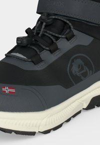 Μαύρο και γκρι παιδικό ορειβατικό μποτάκι με ελαστικά κορδόνια, βόρειο σημαιάκι κοντά στη μύτη και λογότυπο με στυλιζαρισμένο πρόσωπο στο πλάι.