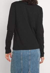 Svart långärmad skjorta i mjukt tyg. Har rund halsringning och sidslitsar. Kombinerad med en blå denimkjol med vertikala sömmar.