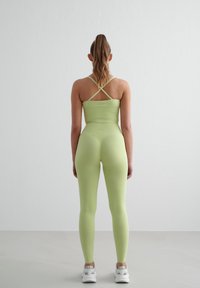 Lysegrønn treningstopp med kryssryggstropper, kombinert med matchende høyt midje leggings. Glatt, elastisk stoff, uten mønstre eller aksenter.