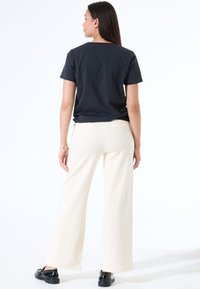 Camiseta negra de manga corta combinada con pantalones de pierna ancha en color crema. El conjunto presenta un corte relajado con una tela suave y sin patrones ni acentos visibles.