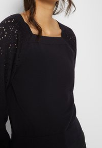 Svart tröja med fyrkantig halsringning, med texturerad stickning på axlarna och långa ärmar. Mjuk tyg med lätt stretch.