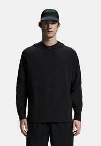 Mustat pitkähihaiset hupparit, jotka on valmistettu sileästä ja kevyestä kankaasta, joissa on kengurulaukku ja resorit, yhdistettynä samanlaiseen mustaan lippikseen.