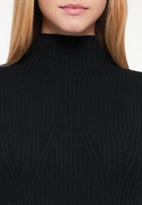 Čierny rebrovaný rolákový sveter s vertikálnymi líniami, s vysokým golierom a priliehavým strihom, vyrobený z textúrovaného pleteného materiálu.