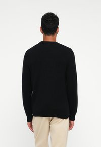Maglione nero lavorato a maglia con scollatura tonda, polsini e orlo a coste. Il tessuto è strutturato, aderente in vita e privo di motivi.