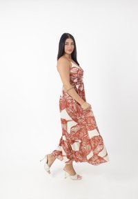 Maxi kjole med en hvid bund og store rustfarvede bladmønstre, en smocket bodice og en flæset kant; parret med åbne hæle.