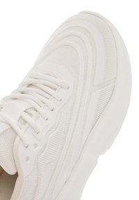 Witte mesh sneaker met een textuurontwerp, een gladde rubberen zool en geïntegreerde veters. Heeft gebogen lijnen en subtiele patroon details.
