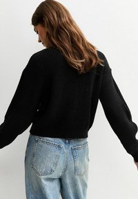 Maglione nero lavorato a maglia con spalle scese e maniche lunghe, abbinato a jeans chiari a vita alta. Tessuto testurizzato con design a coste.