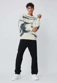 Pull en laine blanc et gris à motifs, coupe décontractée, associé à un pantalon noir ample et des baskets blanches.