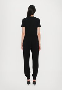 Črna kratka majica s kratkimi rukavi in ujemajoči se jogger hlače. Mehek material, prilegajoč vrh, elastičen pas, usahnila noga in rebrasti manšeti. Čevlji z visokimi petami.